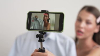 Genç sosyal medyum kadın moda videosu yapıyor. Blogcu kameraya selfie çubuğu ve ışık halkası kullanarak gülümserken, aynı zamanda ikna edici çevrimiçi kıyafetlerin izleyicilere veya takipçilere vlog satmasını sağlıyor. Düzenle