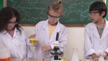 Kafkasyalı öğrenci deney yapıyor ve laboratuvarda yeni yenilikler keşfetmek için bekleyen meraklı çocuklarla çevrili biyokimyasal solüsyon döküyor. Çeşitli mutlu öğrenciler deney yapıyor. Pedagoji.