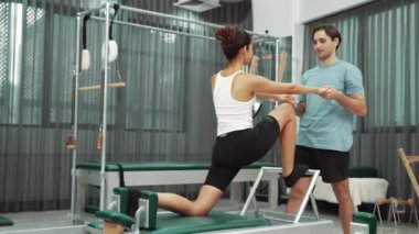 Esneklik ve çekirdek eğitimi için pilates kursunda trapez masasında destek alan bir kadın. Öğrenci dengeyi geliştirmek için reformcuları iki büklüm ediyor. Alışkanlık.