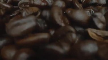 Karışık aromalı kahve çekirdeği yığını masaya saçılmış ve kavrulmuş kahve çekirdekleri etrafa saçılmış siyah arkaplanla çevrilmiş. Makrografi. Ağır çekim. Pabulum.