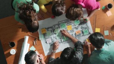 Beyin fırtınası yapmak için yapışkan notlar kullanarak inşaat mühendisi yazma ve planlamasının en üst görüntüsü. Yukarıdan aşağıya iş adamlarının proje planları ve ekipmanlarla masaya not almalarını gösteren bir görüntü. Sempozyum.
