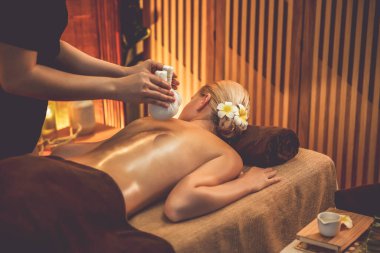 Sıcak bitkisel top spa masaj vücut tedavisi, masör kadın vücuduna nazikçe şifalı bitki torbası bastırıyor. Aromaterapi tesisinin sakinliği ve dinginliği kaplıca salonundaki mumların sıcacık ışığında. Sessiz.