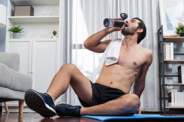Atletik ve sporcu adam spor paspası üzerinde su içiyor. Vücut egzersizlerini bitirdikten sonra evdeki formda ve sağlıklı spor yaşam tarzı için egzersiz yapıyor. Gaiety evde egzersiz eğitimi.