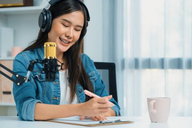 Sosyal medyada kulaklıkla canlı yayın yapan Asyalı sunucu modern stüdyoda yaşam koçluğu veya pazarlama dinleyicilerini selamlıyor. Taktik.