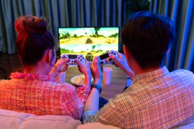 Kontrollü joystickli birkaç oyuncu, televizyon ekranında birlikte araba yarışı oyunu oynuyorlar. Arka tarafta atıştırmalıklar, modern konforlu evinde neon ışıklı oturma odasında kanepe. İnfobahn.