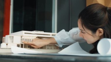 Asyalı genç ve güzel mimar mühendisimiz masaya model konulmuş proje planına bakıyor. Profesyonel proje yöneticisi ev yapısını analiz ediyor. İş tasarımı konsepti. Yönlendirici.