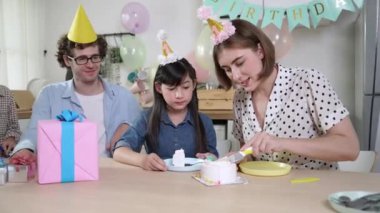 Kafkasyalı anne doğum günü pastasını kesiyor ve babaya verirken tatlıyı ayırıyor. Mutlu aile, kızının doğum gününde masada otururken parti şapkası takar. Özel durum konsepti. Pedagoji.