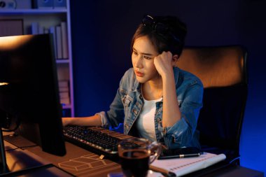 Stresli, genç, güzel Asyalı yaratıcı proje yaratıcısı sosyal medyayı araştırmak için bilgisayara bakıyor ve geceleri daha çok neon modern ofisin planlama kanalı stratejisine ulaşılıyor. Taktik.