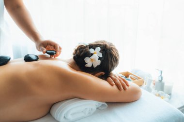 Lüks tatil köyündeki kaplıcalarda sıcak taş masajı. Gün ışığı sükunet ortamında, mutlu kadın müşteri bazalt taş masajından zevk alıyor. Rahatlatıcı bir sıcaklıkla vücudun üzerinde süzülüyor. Sessiz.