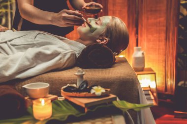 Kaplıca salonunun sakin atmosferi, kadın müşteri sıcak mum ve lüks yüz kremi masajıyla kendini yenileme zevkine kapılıyor. Yüz bakımı ve güzellik konsepti. Sessiz.