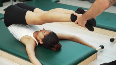 Pilates müşterisi pilates minderinde yuvarlanırken bacak kaldırma alıştırması yapıyor. Kadın, karın bölgesini güçlendirmek ve esnekliği artırmak için antrenörlük yaparken ters duruşta poz veriyor. Alışkanlık.