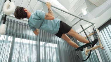 Çekirdek dayanıklılığı ve spor salonunda vücut egzersizi için pilates trapez masasına tırmanan bir adam. Eğitmen, arka ve kalça esnekliğini arttırmak için Cadillac 'ta ters asılı duruyor. Alışkanlık.