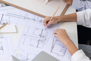 Asyalı kooperatif iş arkadaşı ev modelini ev modeliyle ve bina planıyla birlikte masaya koyarken, profesyonel güzel mimarın el yapımı taslaklarının en üst görüntüsü. Tertemiz..