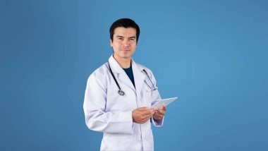 Laboratuvar önlüğü ve steteskobu olan ve mavi arka planda duran profesyonel bir doktor. Kameraya poz verirken tıbbi verilere bakıp kontrol eden yetenekli bir sağlık çalışanı. Yaratıcılık.