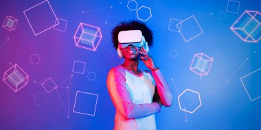 VR gözlüklü Afrikalı kız mavi ve pembe arka planda duruyor ve yüzen geometrik şekle bakıyor. Heyecanlı insan görsel gerçeklik dünyasına giriyor. Teknoloji yeniliği. Yaratıcılık.