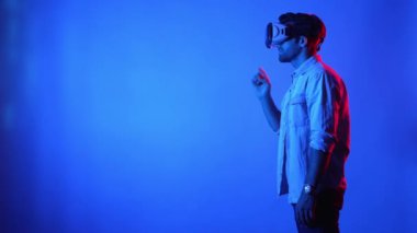 Sanal gerçeklik gözlüğünü açıp hologramı araklayan sıradan giysili iş adamının yan görüntüsü. Üstveriye erişip girerken mavi arka planda duran yetenekli erkek model. Teknoloji. Aygıt.