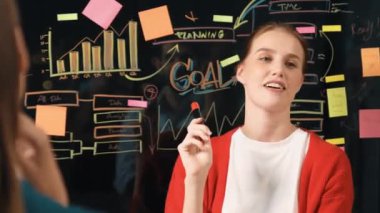 Profesyonel iş kadını yapışkan notlar ve grafikler kullanarak kendine güvenen bir iş kadını sunar. Cam duvarda istatistiksel grafikle duran yetenekli genç ve güzel proje yöneticisi. İzleme