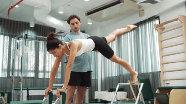 Bir pilates eğitmeni, müşteriye bir ıslah makinesinin tahta varyasyonunda rehberlik eder. Sağlıklı bir kadın, dengeyi geliştirmek için antrenör yardımı ile yenilikçi üzerinde yan kalas değişimi yapıyor. Alışkanlık.