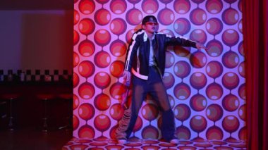 Asyalı break dansçı serbest stile geçiyor ve balon arka planlı kameraya bakıyor. Profesyonel hippi gündelik kıyafet giyer ve gözlük takar. Mutluluk.