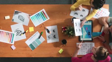 Proje yöneticisi renk paletleri seçerken tasarımcının tablete baktığı yukarıdan aşağıya hava görüntüsü. Profesyonel grafik tasarımının en üst görüntüsü ve logoya bakın. Yetenekli ekip grafikleri seçiyor. Sempozyum.