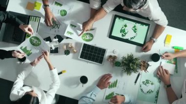 İş adamlarının rüzgar değirmeniyle toplantı masasında temiz enerji ve sürdürülebilir yatırım kullanımı, çevre grafiği ve ahşap ev modeli ile ilgili tartışmalarına tepeden aşağı bakış açısı. Hizalama.