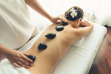 Lüks tatil köyündeki kaplıcalarda sıcak taş masajı. Gün ışığı sükunet ortamında, mutlu kadın müşteri bazalt taş masajından zevk alıyor. Rahatlatıcı bir sıcaklıkla vücudun üzerinde süzülüyor. Sessiz.