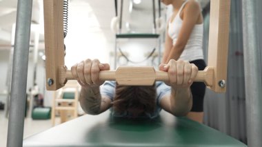 Eğitmen rehberliğinde Pilates Cadillac üzerine bar tabanlı alıştırma yapan bir müşteri. Erkek öğrenci, üst vücut gücünü arttırmak için Cadillac 'ın üzerinde kuğu esnetiyor. Alışkanlık.