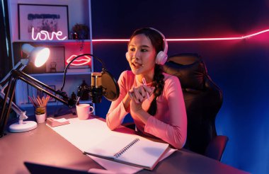 Geceleri podcast 'te olumlu konuşmalar yapan, pembe neon ışıklı modern stüdyoda sunum için dizüstü bilgisayar kullanan, gülümseyen, genç, güzel Asyalı bir etkileyiciydi. Taktik.