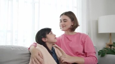 Kafkasyalı anne kızını kucaklıyor ve kanepede oturuyor ve alnından öpüyor. Mutlu anne oturma odasında sevimli Asyalı liseli kıza sevgi ve sevgi gösteriyor. Güzel bir aile birlikte vakit geçirir. Pedagoji.