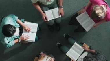 Katlanmış eller yaparken, kucağında haçla İncil okuyan duaların en üstteki görüntüsü. İnanç, güven ve umutla Tanrı 'ya dua eden farklı insanların havadan görünüşü. Ve daireler çizerek oturuyor. Sempozyum.