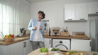 Mutlu baba yemek pişirirken müziğe geçiyor ve modern mutfakta öğle yemeği hazırlıyor. Aktif baba, sebze ve mutfak gereçleri ile çevrili sağlıklı yemek ya da salata yaparken şarkıyla dans ediyor. Pedagoji.