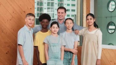 Mutlu öğretmen ve çeşitli öğrenciler kameraya gülümserken ayakta duruyorlar. Profesyonel akıllı eğitmen ve karışık ırk olan lise öğrencileri kameraya neşeli pozlar veriyor. Öğretim