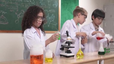 Çocuklar laboratuvarda karatahta başında dururken fen dersinde deney yapıyorlar. Mutlu öğrenci biyokimyasal sıvıyı keşfederken ve incelerken ve karıştırırken. Pedagoji.