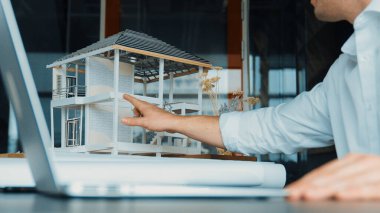 Kabiliyetli beyaz mimar el yapımı ev tasarımını dizüstü bilgisayardaki model ve plan ile karşılaştırın. Dizüstü bilgisayar kullanan profesyonel proje yöneticisi. Eline odaklan. Yönlendirici.
