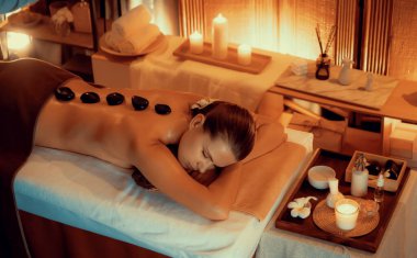 Lüks tatil köyündeki kaplıcalarda sıcak taş masajı, sıcak mum ışığı, spa bazalt taşı masajının keyfini çıkaran mutlu kadın müşteriler, rahatlatıcı bir sıcaklıkla vücudun üzerinde süzülüyorlar. Sessiz.