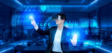 VR gözlüklü bir proje yöneticisi mali tabloyu ve ofisteki parlak mavi ışığı gösteriyor. Yetenekli iş adamı artırılmış gerçeklikten elde edilen verileri kullanarak pazarlama stratejisini kontrol edip planlıyor. Yaratıcılık.