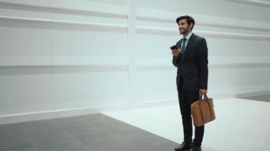 Yetenekli yönetici, iş arkadaşıyla proje hakkında konuşmak için telefon görüşmesi yapıyor. Yakışıklı erkek lider, beyaz arka planda yürürken haber vermek ve cep telefonunu cebe indirmek için iş ekibini arıyor. Sevinçli..