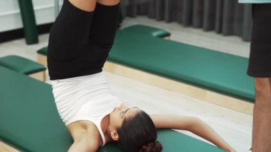 Pilates müşterisi pilates minderinde yuvarlanırken bacak kaldırma alıştırması yapıyor. Kadın, karın bölgesini güçlendirmek ve esnekliği artırmak için antrenörlük yaparken ters duruşta poz veriyor. Alışkanlık.