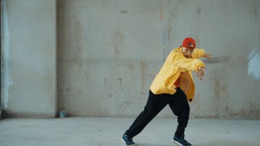 Beyaz hipster sokak, şehir merkezinde ayak sesleri gösteriyor ya da pratik yapıyor. Hareketli genç break dansçı hareketi ve kol ve bacak esneme hareketi. Açık hava sporu 2024. Gri arka plan. Hiphop.