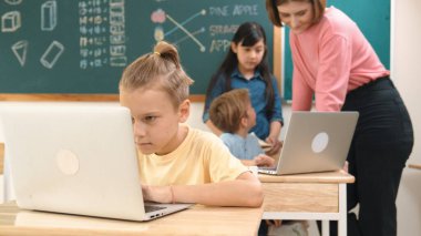 Kafkasyalı çocuk çeşitli öğrenci kodlama mühendisliği programlarıyla çevrili program yazarken programlama sistemine odaklanıyor. Happy öğretmen bilgisayar dersinde dizüstü bilgisayarda çalışan çocuklara destek oluyor. Pedagoji.