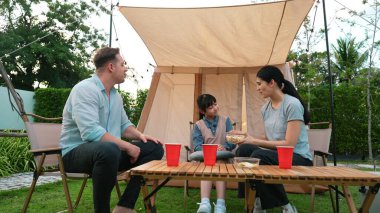 Aile hep birlikte bahçedeki kampta oturup yemek yiyor. Sevimli ebeveynler, genç nesil arasında iletişim kurmak ve zaman geçirmek için açık hava kamp faaliyetlerini kullanırlar. Uyumsuzluk.