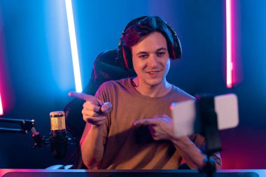 Oyun kanalı, online oyun oynayan akıllı flamalı oyun sunucusu, kulaklık takan, neon ışıklandırma odasındaki takım oyuncusuyla akıllı telefondan canlı yayında konuşan izleyiciler. Bireysel.