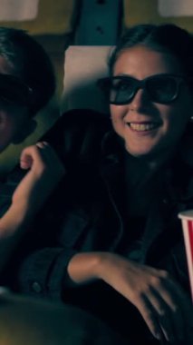 Sinemada üç boyutlu gözlüklü bir kadın ve erkek film izliyor. Ekrana bakar, heyecan verici ve patlamış mısır yer.