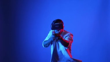 VR gözlüklü oyuncu sanal dünyaya girerken silah tutuşu yapıyor ve atış oyunu oynuyor. Mavi arka planda dururken simülasyon dünyasında zırh tutan yetenekli bir adam. Aygıt.