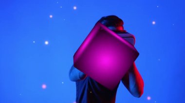 Meta evreni bağlamak için VR gözlük takarken yetenekli oyuncu boksörleri ve yüzen kutuları yumrukluyor. Erkek model, egzersiz yaparken ve neon arka planda dururken sanal gerçeklik gözlüğü kullanıyor. Aygıt.