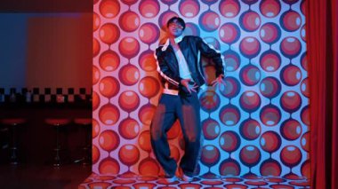 Asyalı break dansçı serbest stile geçiyor ve balon arka planlı kameraya bakıyor. Profesyonel hippi gündelik kıyafet giyer ve gözlük takar. Mutluluk.