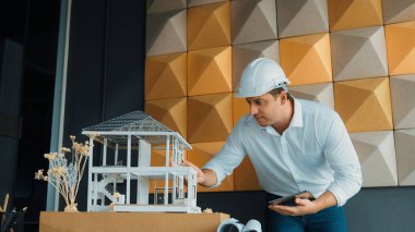 Tablet analiz evi inşaatı kullanan profesyonel beyaz mimar mühendisi ve toplantı masasına yerleştirilmiş mimari model ve ekipman ile model yapısını dikkatlice kontrol ediyor. Yönlendirici.