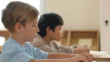 Beyaz tenli ilkokul öğrencisinin tahtada otururken bir nota bakması ve soruya cevap vermesi. Çocuklar derse katılırken genç öğretmen sınıf çalışmasını ya da sınavı açıklar. Pedagoji.