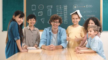 Profesyonel Kafkas öğretmeni ve çeşitli öğrenciler kameraya bakarken mutlu çocuk başparmak gösteriyor. Sınıfın önünde dururken gülümseyen bir grup çok kültürlü çocuk. Eğitim. Pedagoji.