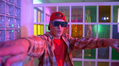 Komik break dansçı kameraya bakarken hip hop 'a doğru serbest adım atıyor. Çılgın mutlu hipster dans edip sokak dansı yaparken Led ışığında günlük kıyafet ve güneş gözlüğü takıyor. Mutluluk.